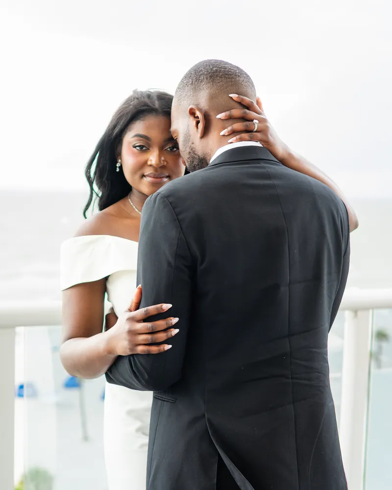 A bride and groom embrace on a balcony overlooking the water.